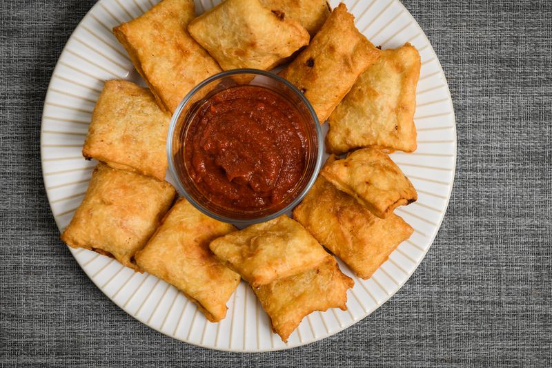 Homemade pizza rolls on a plate alongside a small dish of red dipping sauce.