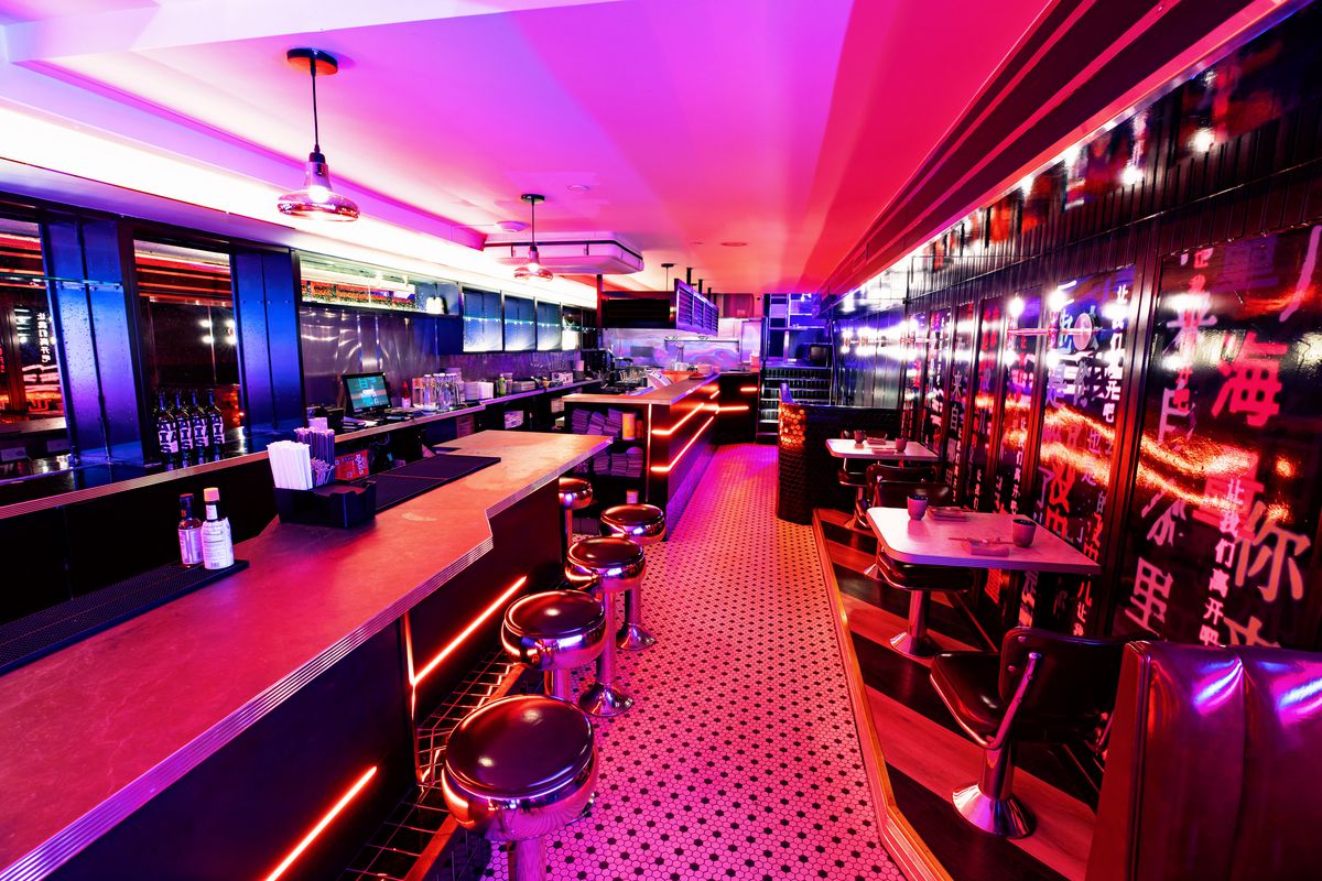 A dimly neon lit restaurant with wide tables and chairs. 