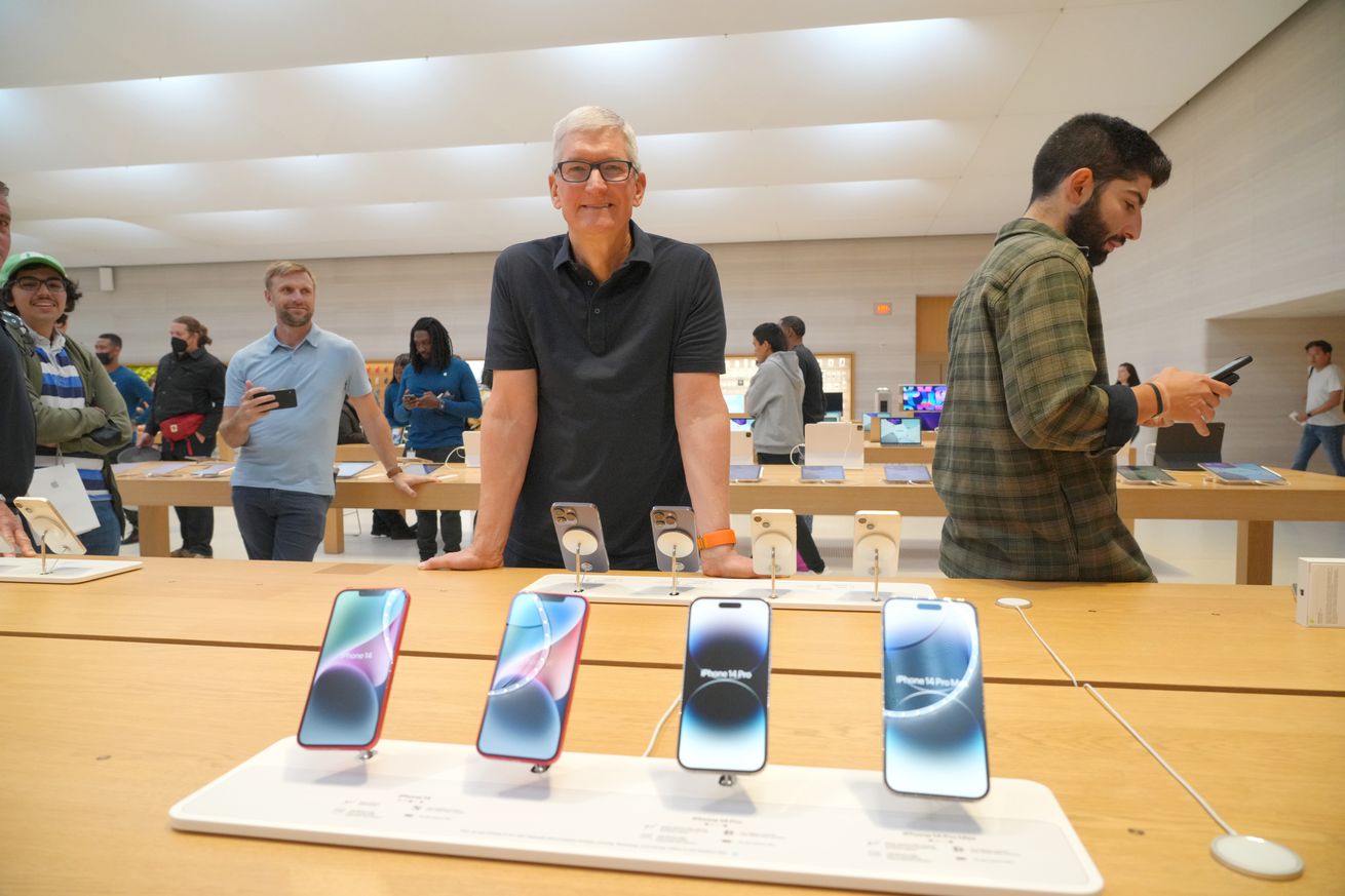 Tim Cook stands over several iPhone 14 devices.
