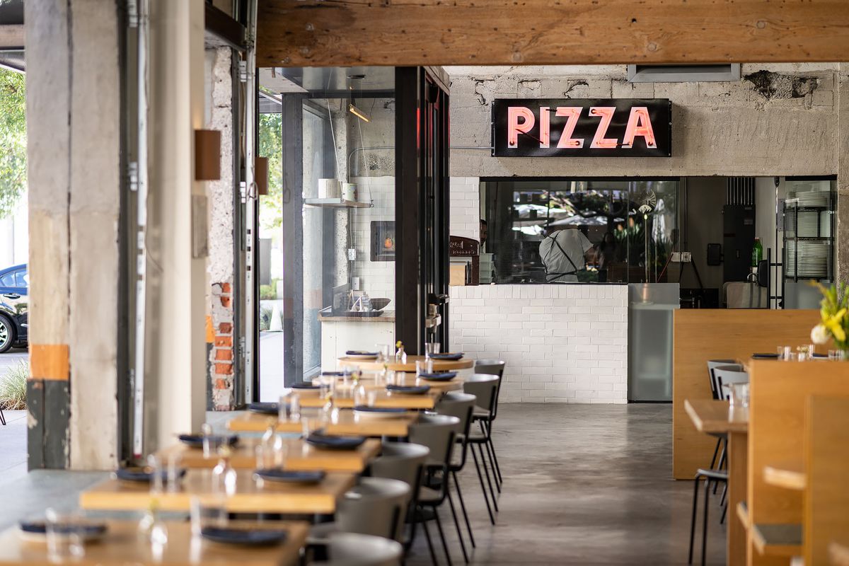 An industrial dining room with concrete, white walls, and a pizza sign at Pizzeria Bianco.