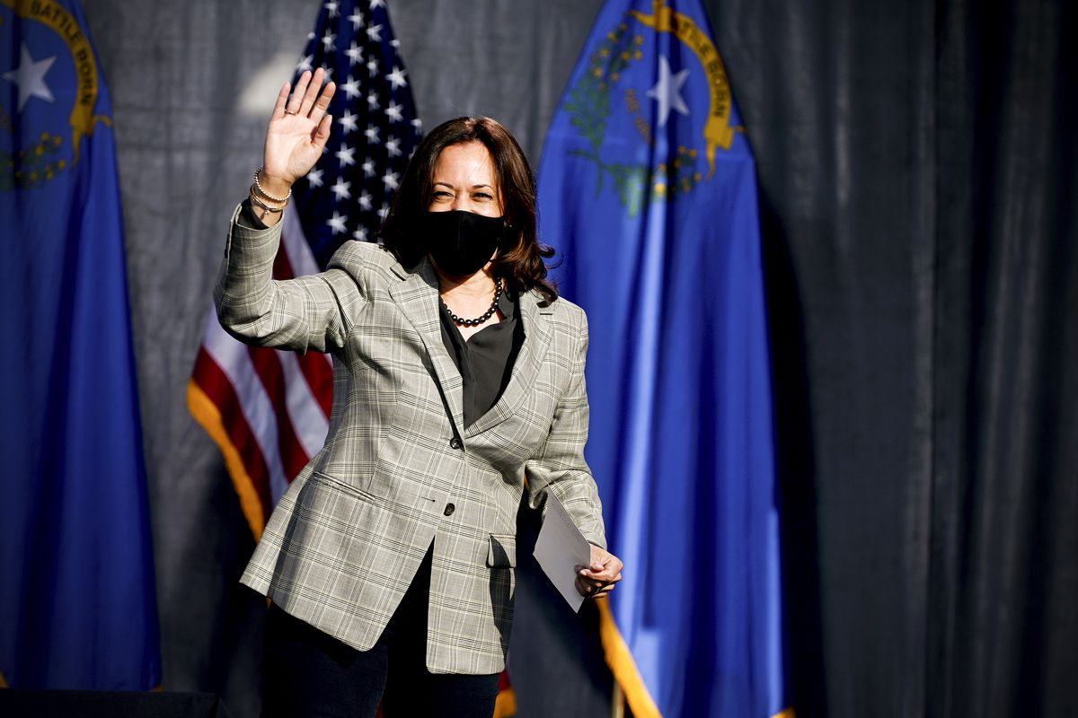 Kamala Harris wears a face mask and waves to an unseen audience as she walks onto a stage