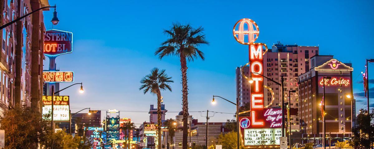 A sunset view of a main street and neon-lit signs in Downtown Las Vegas.