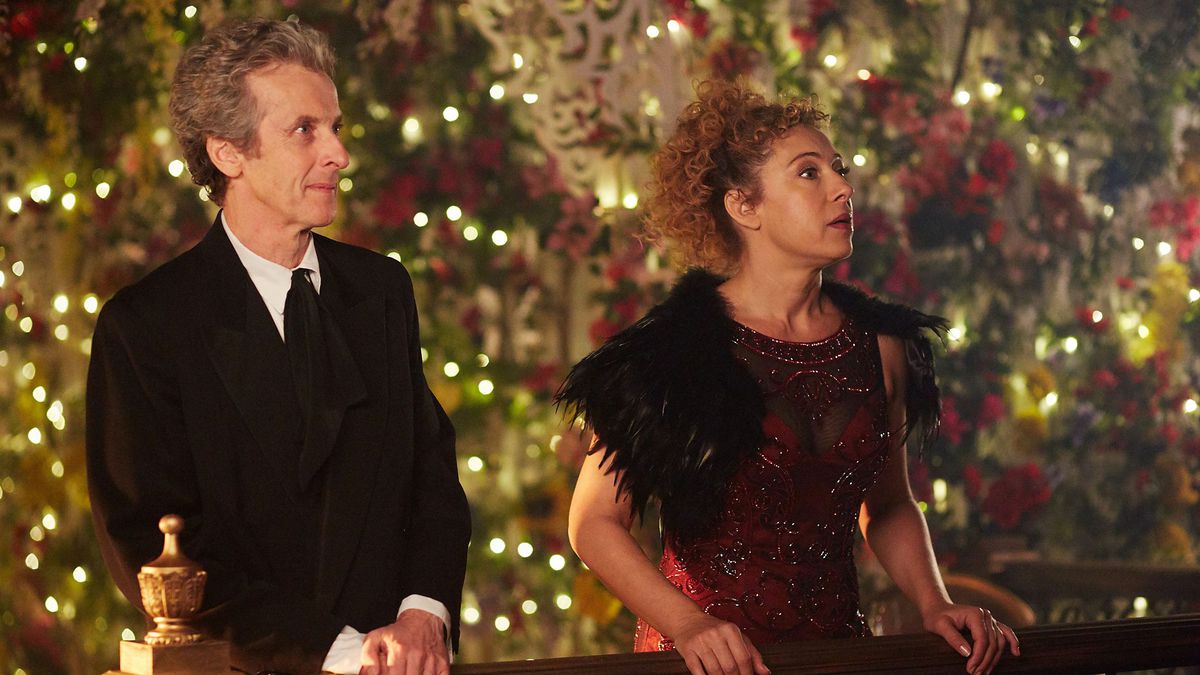 The Twelfth Doctor and River Song stand in front of a Christmas tree