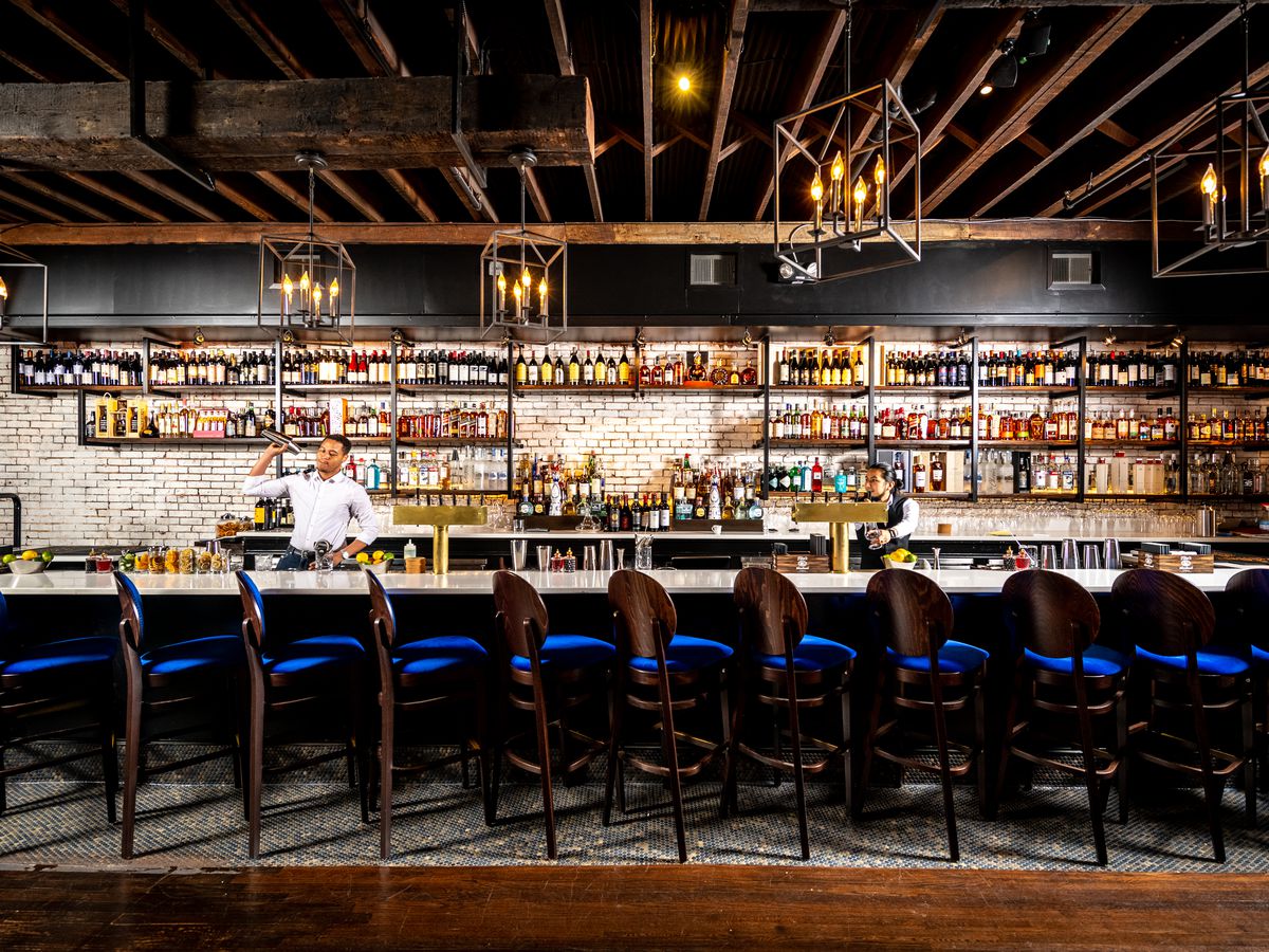 A lengthy bar lined in brick and blue bar stools