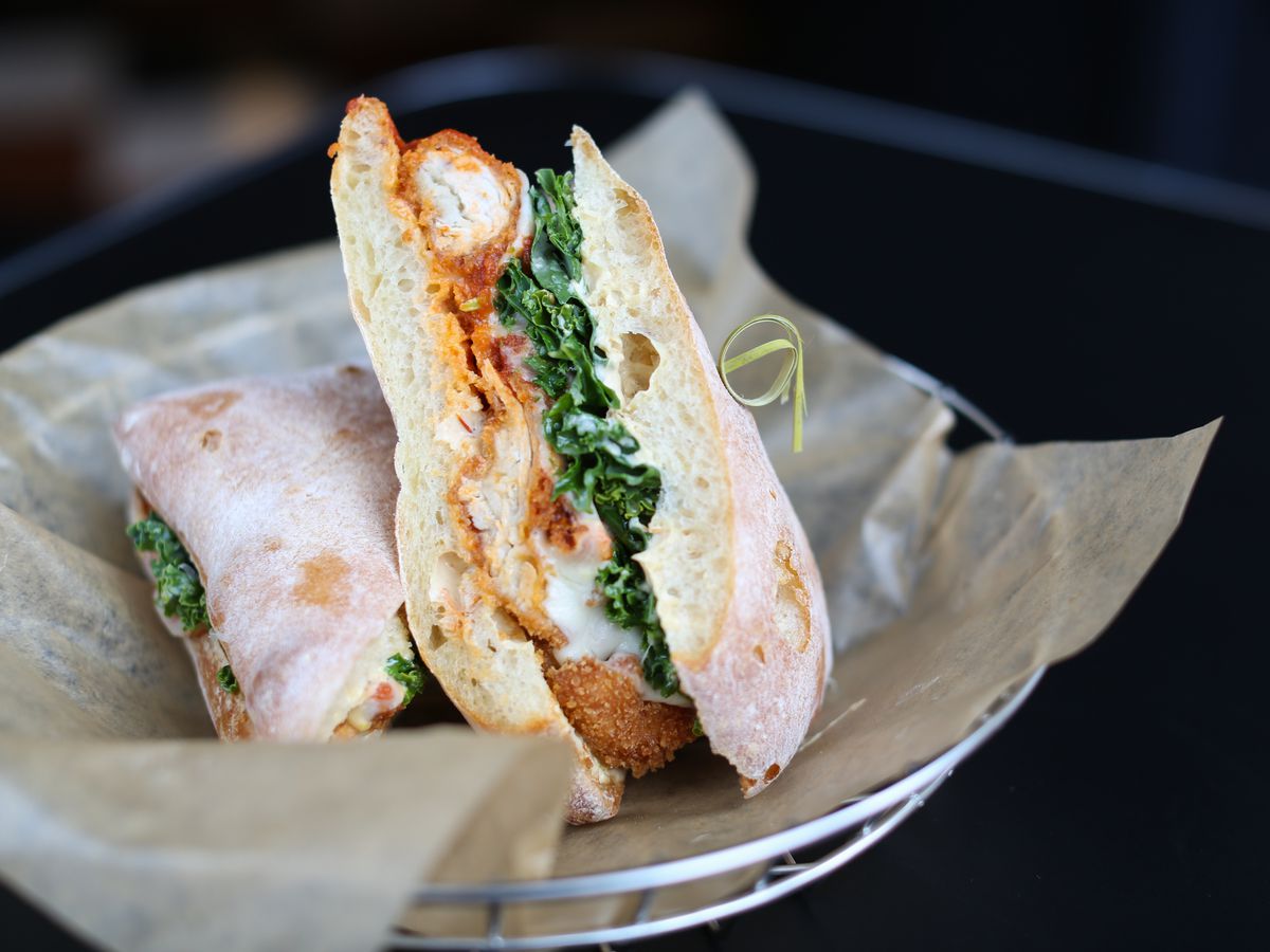 A breaded chicken sandwich with greens and mayo on thick bread, skewered, and served in a paper-lined basket