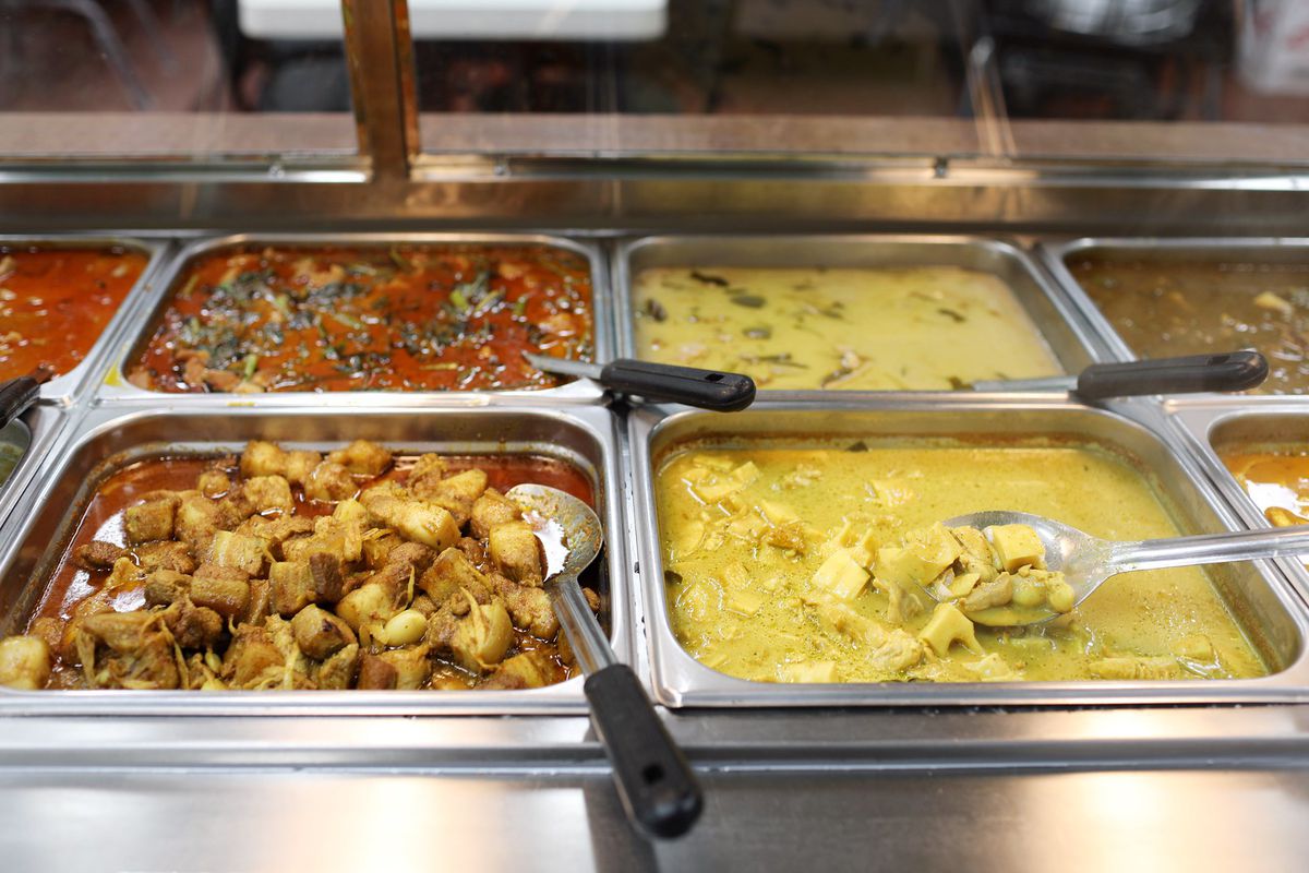 A steam table with four compartments filled with curry. The two on the left are reddish while the two on the right are yellow