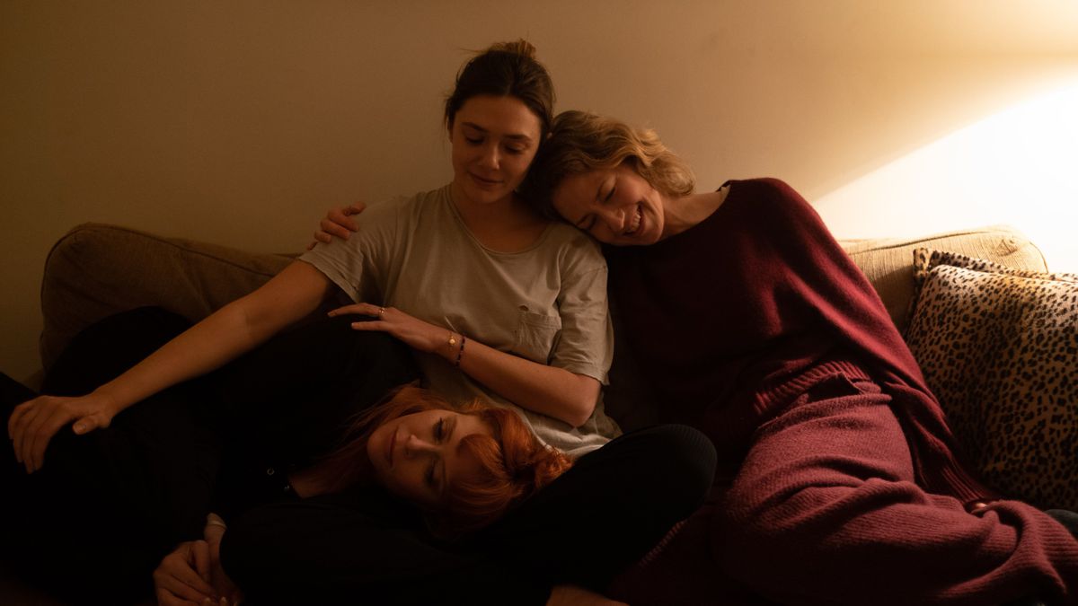 Three women sit on a couch, huddled close to one another.