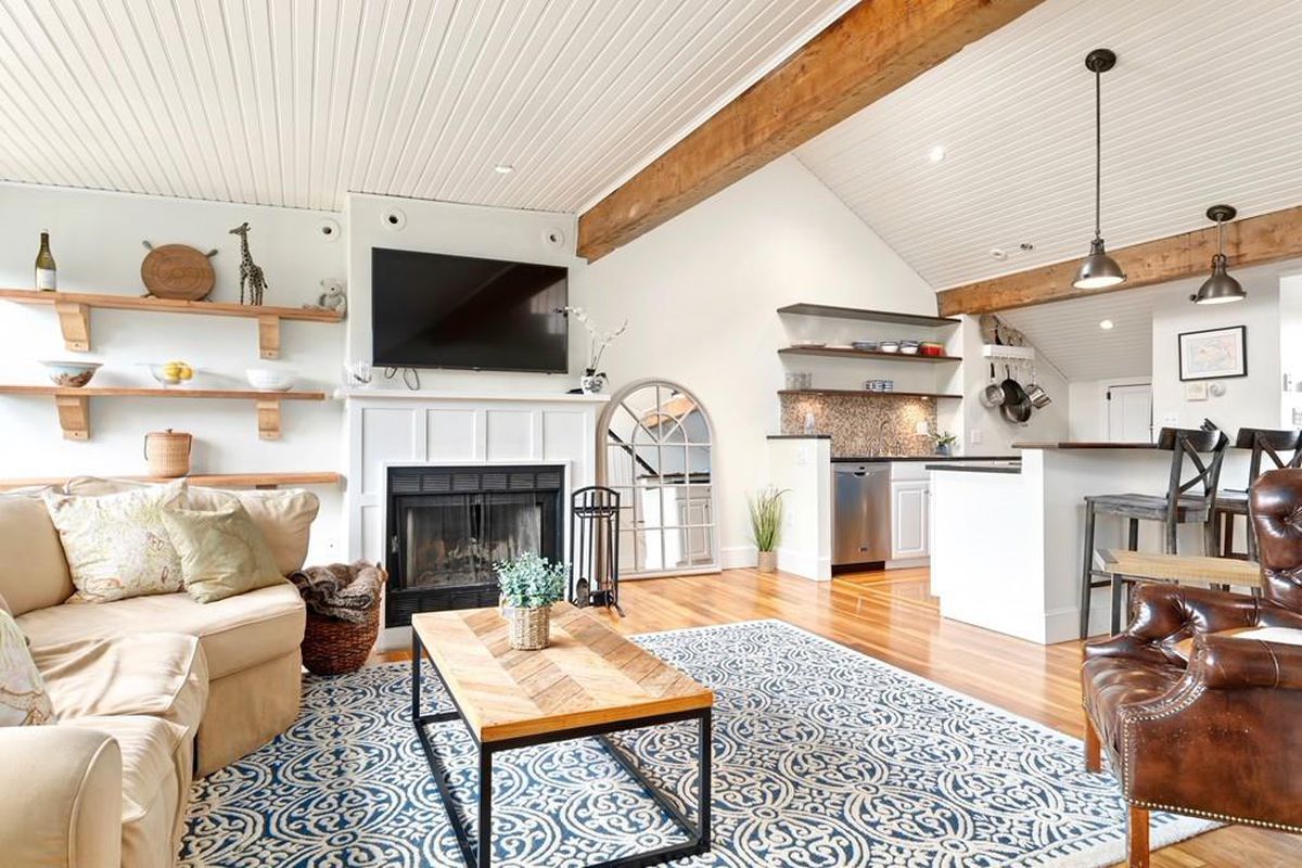 An open living room with furniture and a fireplace, and exposed beams on the vaulted ceiling.