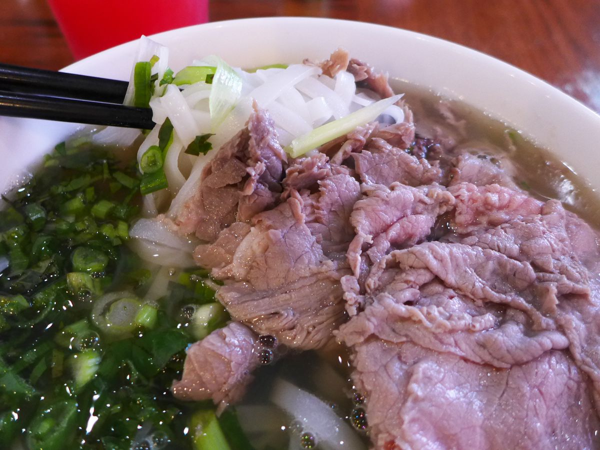 A pho with lots of green onions, and some very nice sliced beef cooking on the top of the broth.
