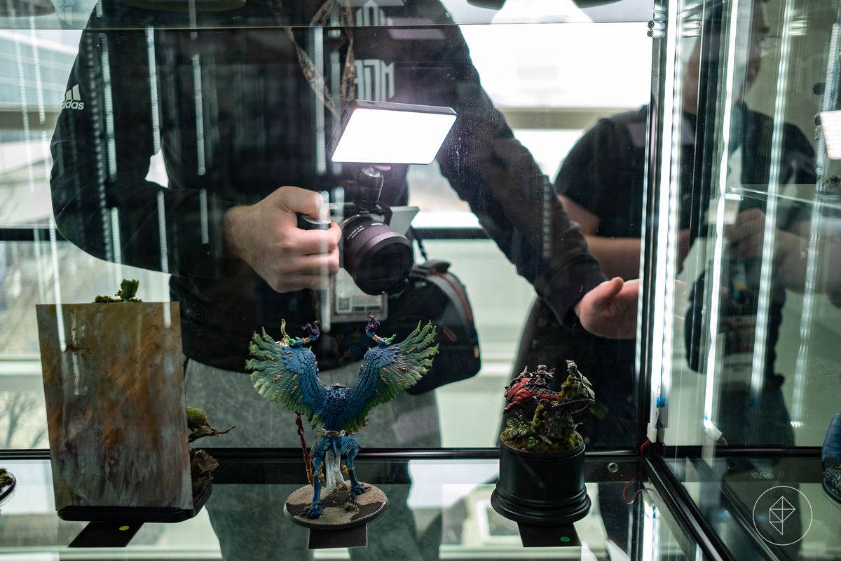 A photographer with lighting takes pictures through the glass cases at AdeptiCon 2023.