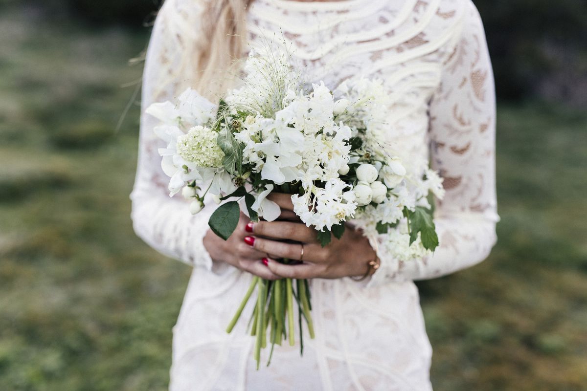 A bride wearing a lace long-sleeve wedding dress, holding flowers
