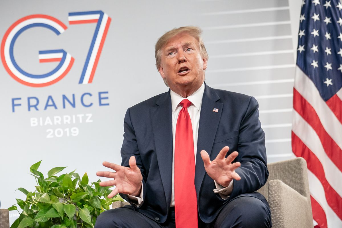 President Donald Trump holds his hands out while sitting on the G7 summit stage.
