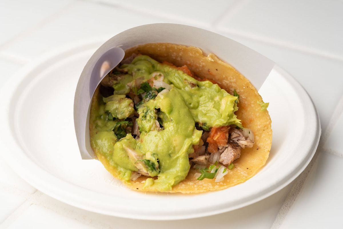 A carne asada taco slathered in guacamole and wrapped in a corn tortilla and paper.