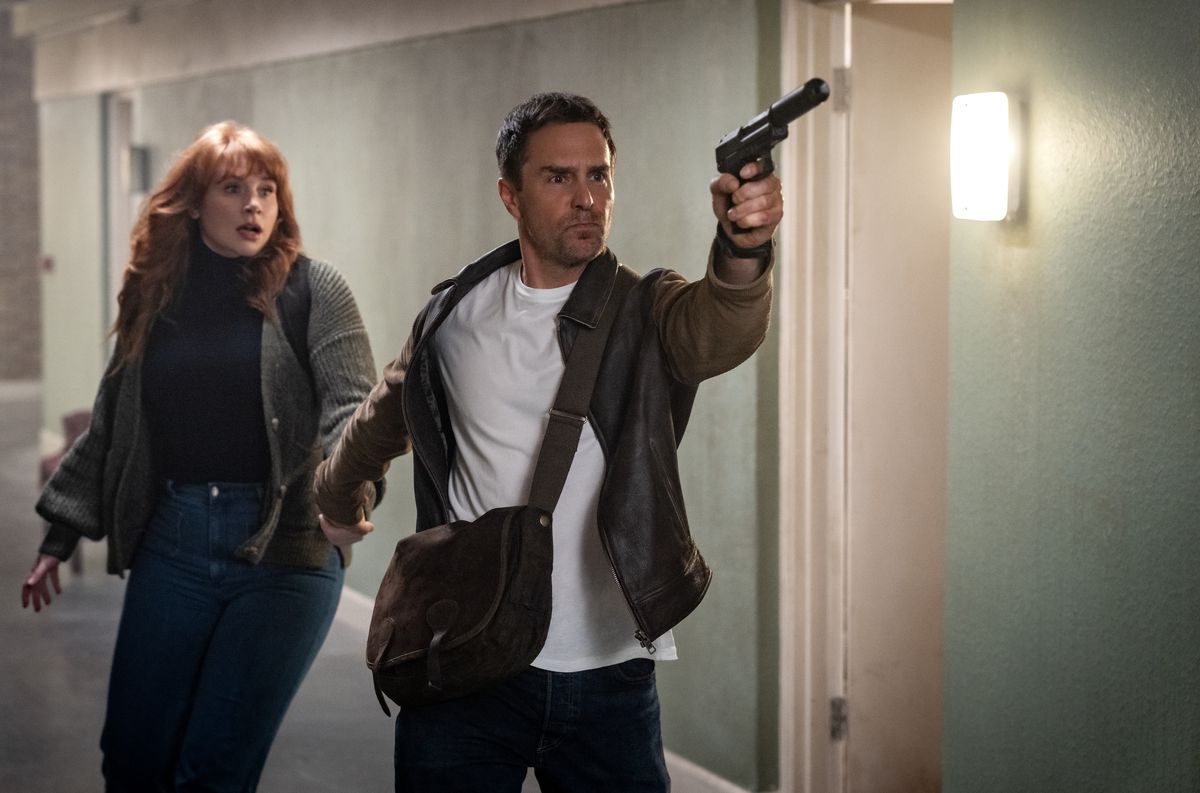 Sam Rockwell, brandishing a silenced pistol, leads a scared-looking Bryce Dallas Howard down a corridor in Argylle