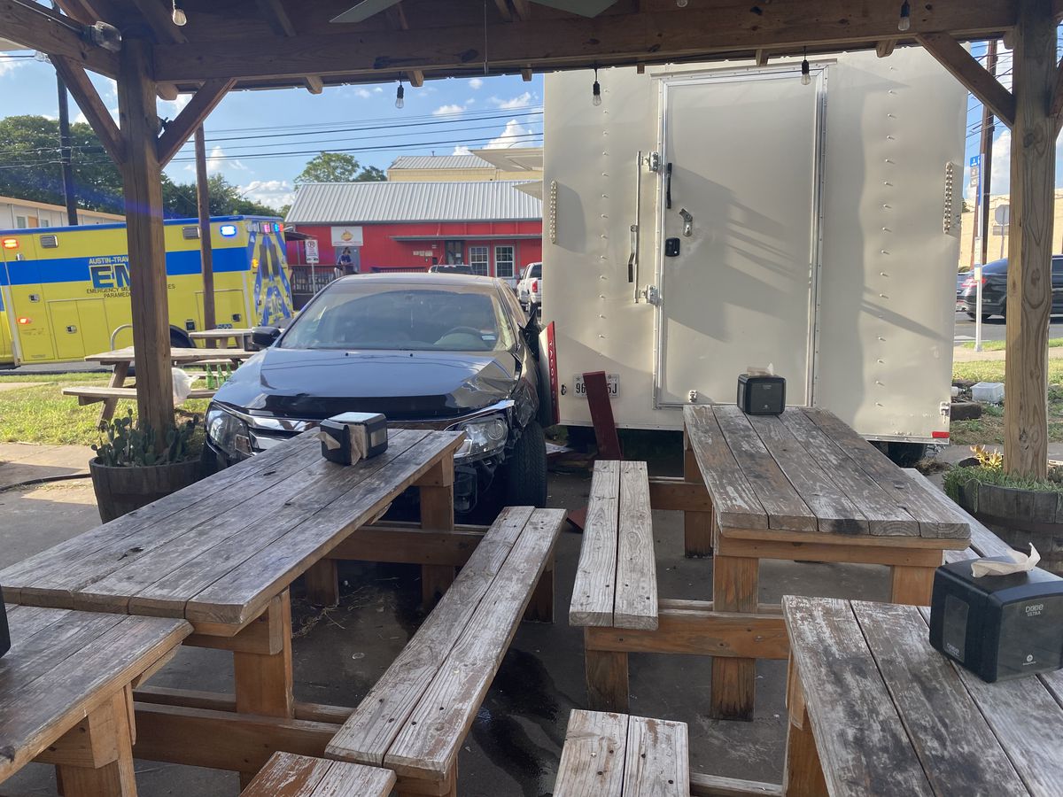 A black car crashed into the outdoor dining area of a food truck with picnic tables