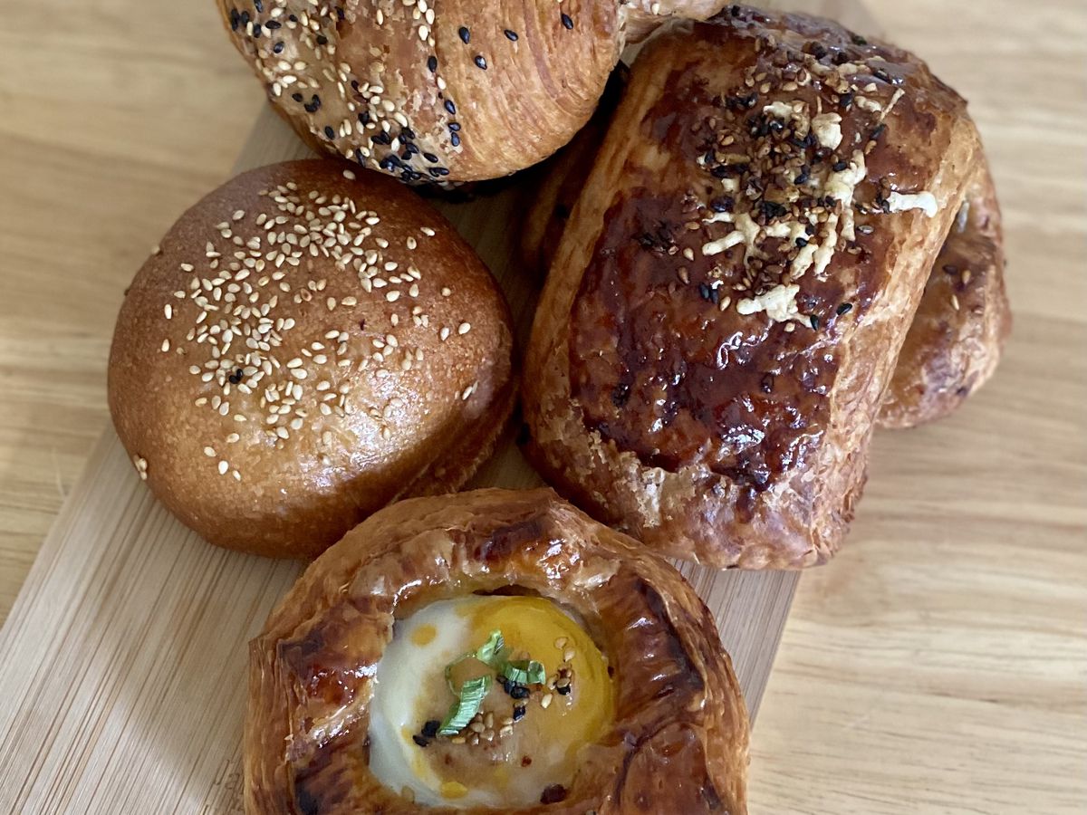 Four pastries on a wooden table including a Danish topped with an egg and a croissant covered in everything bagel seasoning.