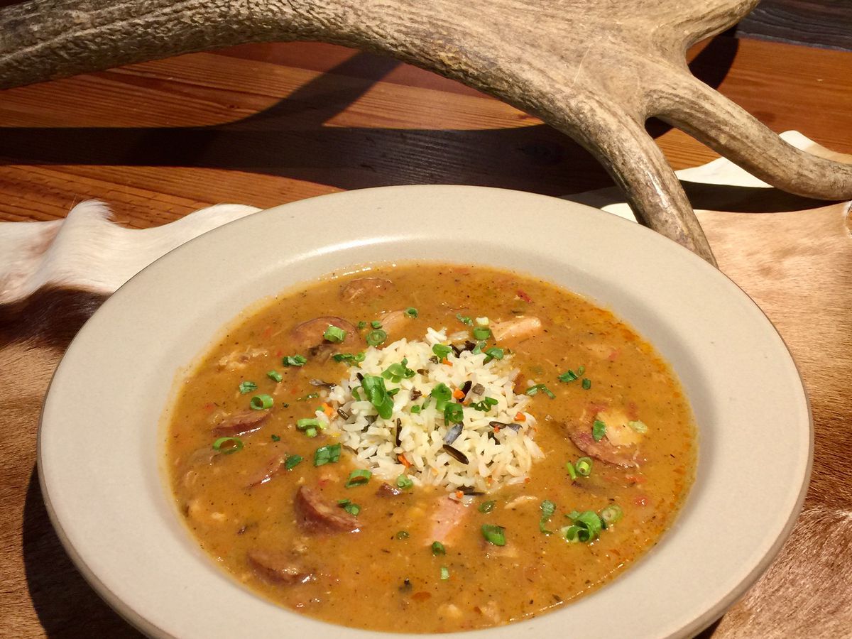 A bowl of smoked duck gumbo topped with wild rice pilaf in a white bowl.