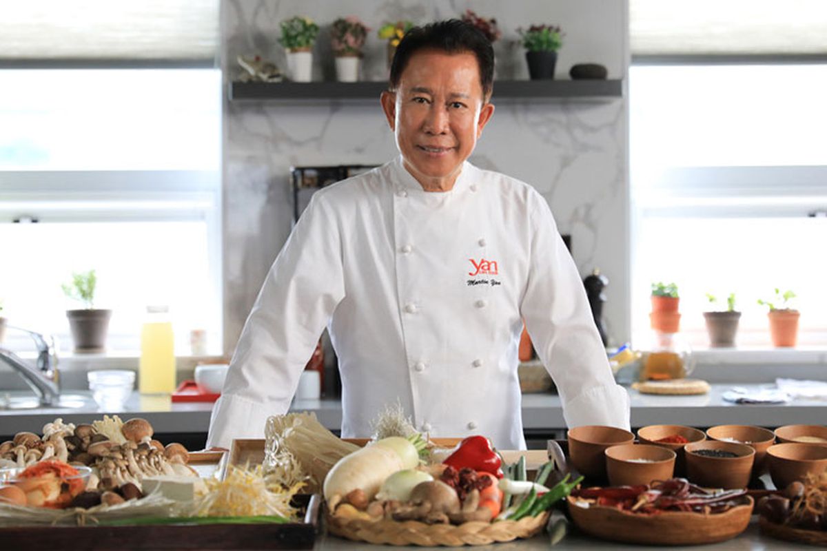 A man in a white chef’s coat stands in front of a counter with food on it. 