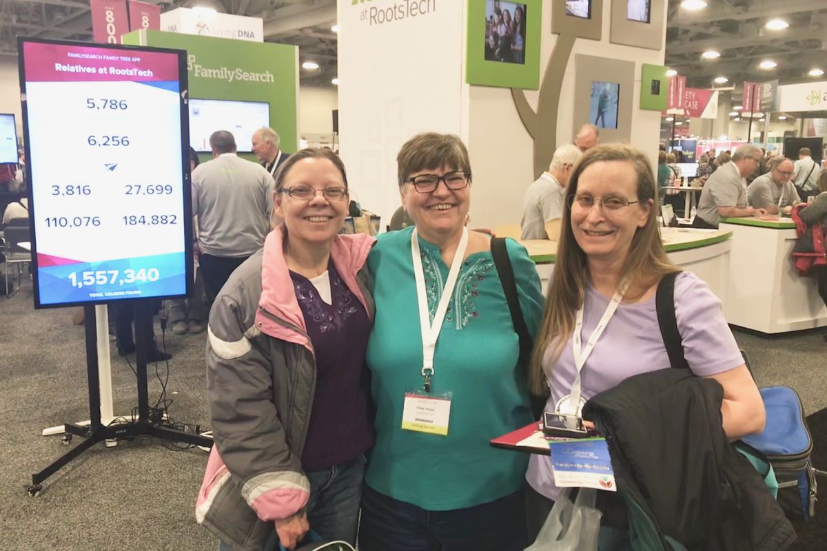 Sisters Stephanie Rask, left, and Sher Huss, middle, met their fourth cousin Glenda Ferran, right, at the FamilySearch booth in the Expo Hall at RootsTech on Thursday. They stand next to a screen displaying the total number of cousins who have been found 
