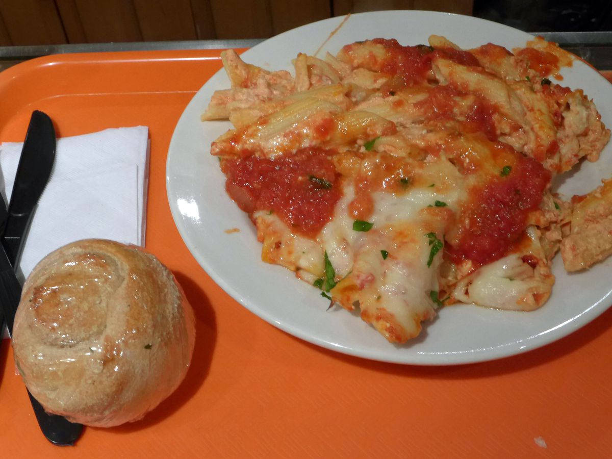 A gooey plate of baked pasta with a plastic wrapped roll on the side
