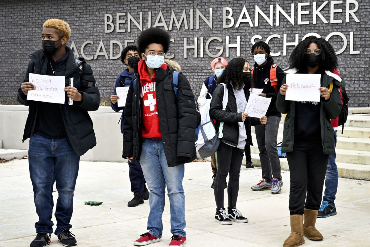 Students stand in front of a high school holding protest signs.