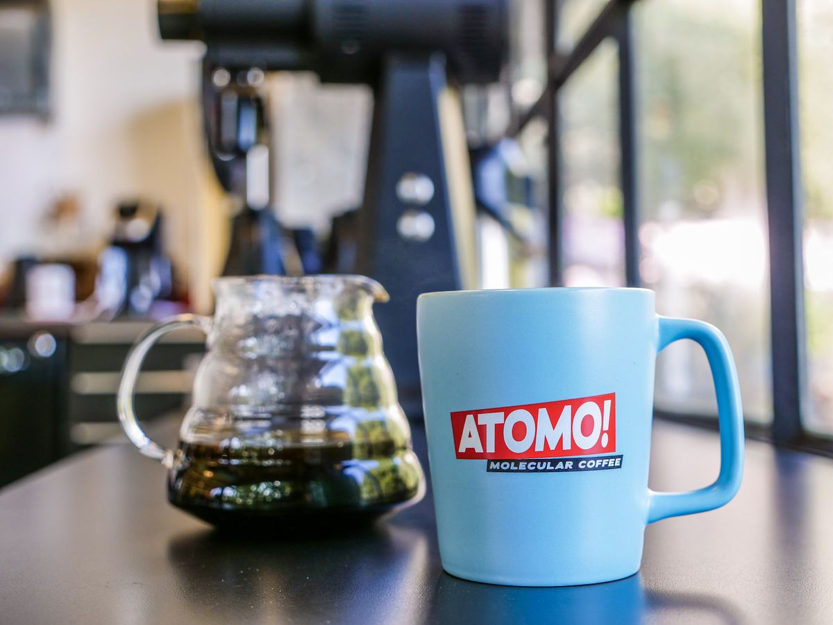 A closeup of a blue Atomo mug with a glass pitcher of coffee to the left.