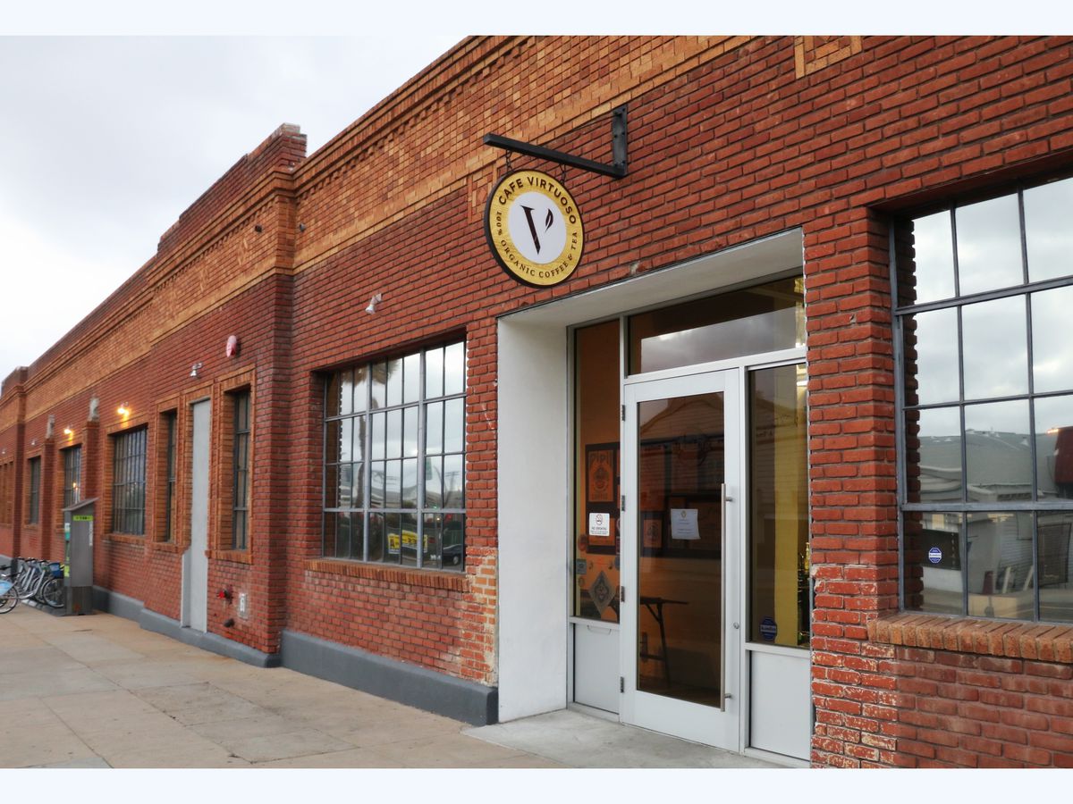 The brick storefront of Cafe Virtuoso, with the black and yellow logo hanging above the door.