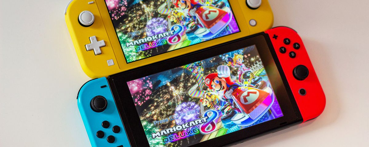A photo comparing the smaller Switch Lite with the slightly bigger standard Switch model. Both Switches are displaying the Mario Kart 8 main menu.