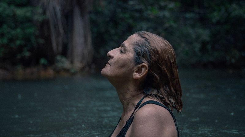 A Brazilian woman is swimming, and has slicked back her hair and has her eyes closed.
