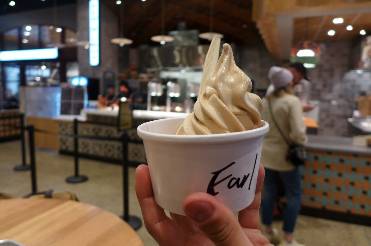 A hand holds a curly serving of beige soft serve aloft.