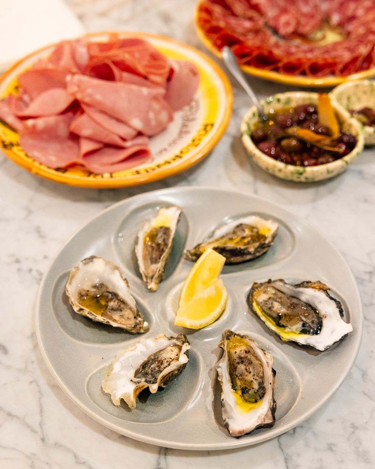 A plate of oysters next to plates of Italian sliced meats.