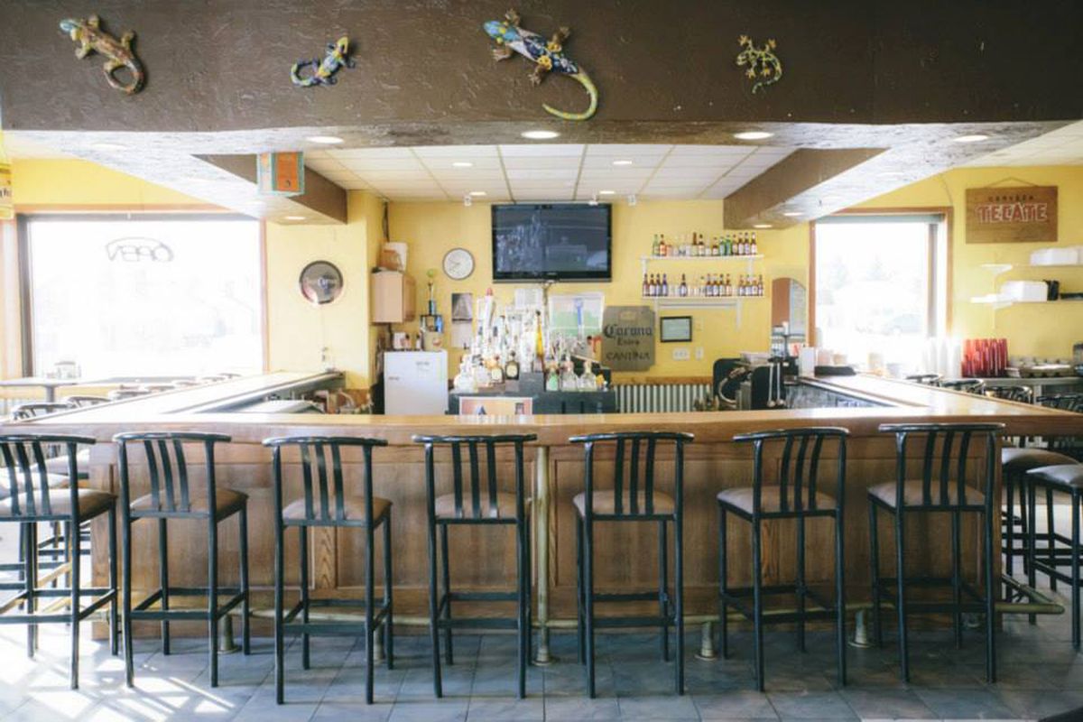 A bar with black chairs and yellow walls with Corona beer signs. 
