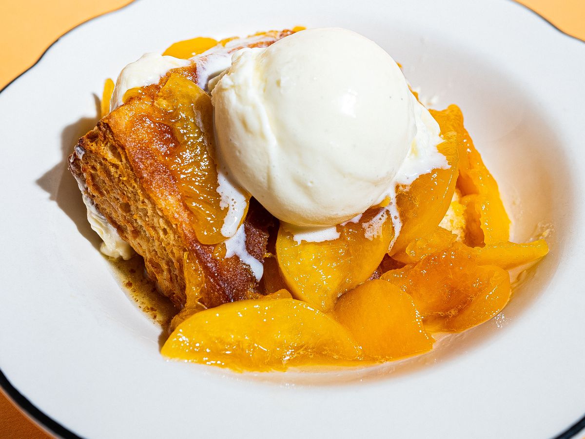 Peaches and a biscuit topped with ice cream in a white bowl. 