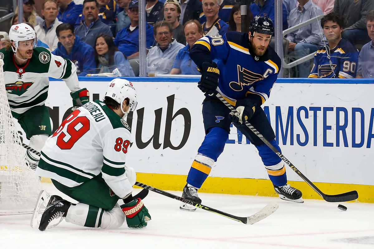 Ryan O’Reilly of the St. Louis Blues looks to pass the puck while under pressure from Frederick Gaudreau and Jon Merrill of the Minnesota Wild during the third period in Game Six of the First Round of the 2022 Stanley Cup Playoff at the Enterprise Center on May 12, 2022 in St Louis, Missouri.