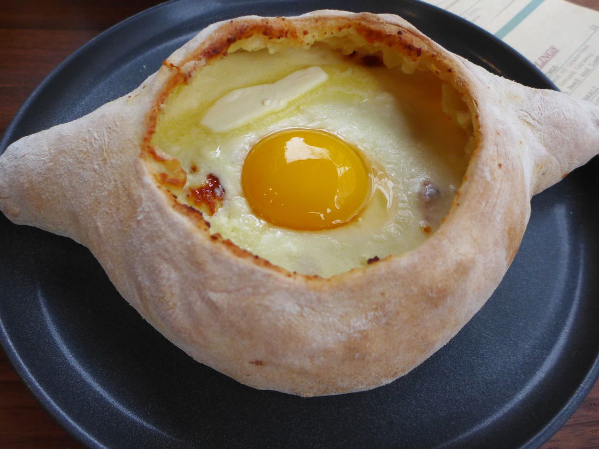 A round bread with two opposing bread handles and cheese and an uncooked egg yolk in a pool in the middle.