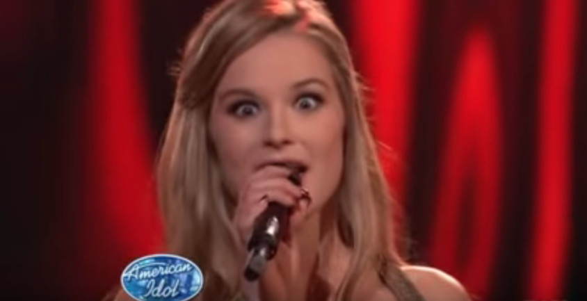 Photo of a blond woman with her eyes bugged out singing into a microphone