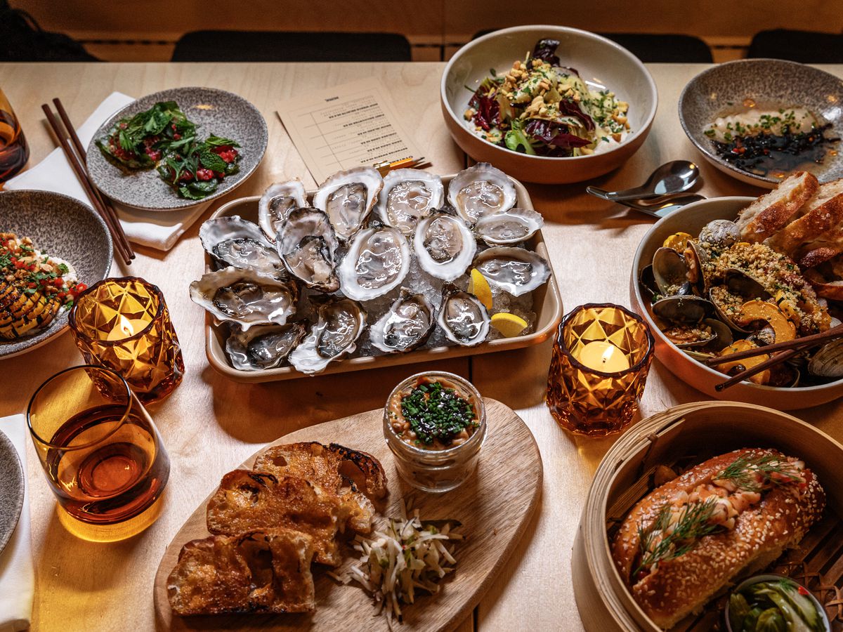 The spread of oysters and other small plates surrounded by chopsticks and amber colors glasses and candle holders at Mink.