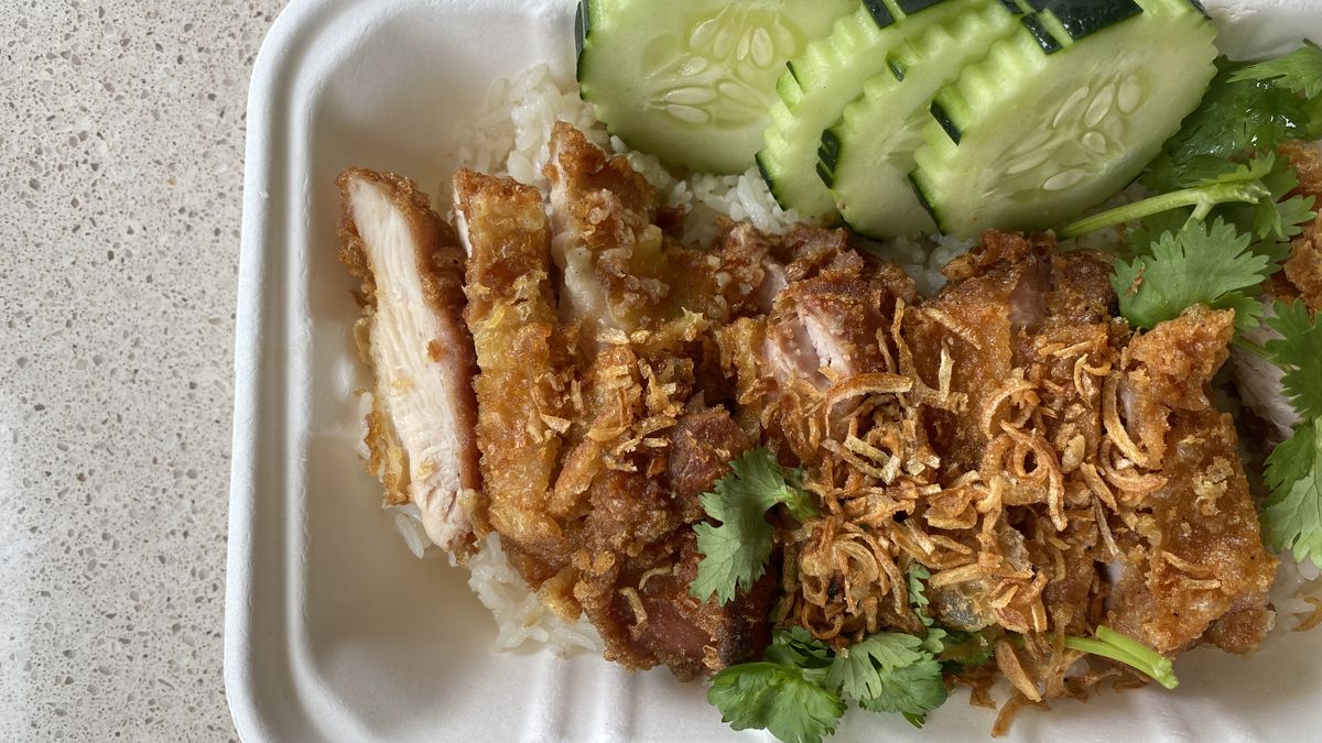 Sliced golden fried chicken sits next to cucumbers and over a pile of rice; springs of verdant cilantro are scattered about