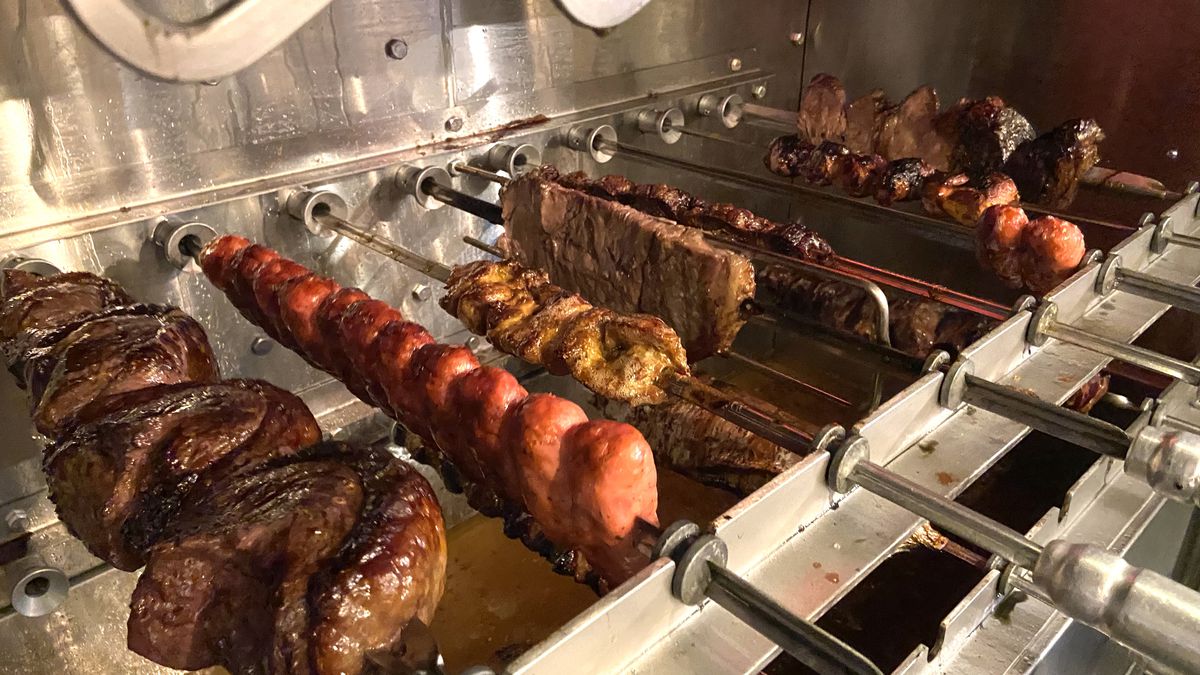 Skewers of meat are lined up on spits, photographed at an angle.