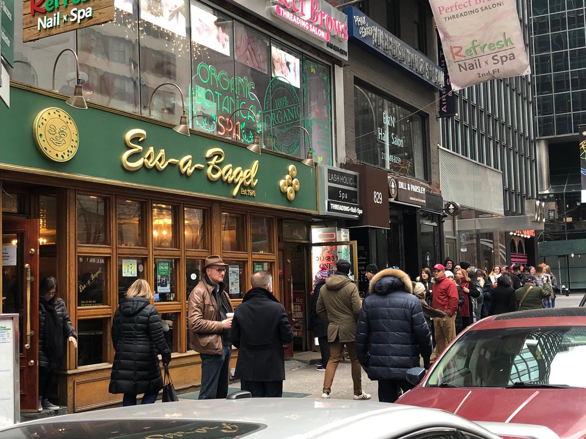 A wooden exterior of a bagel shop with green signage on a busy street in Midtown.