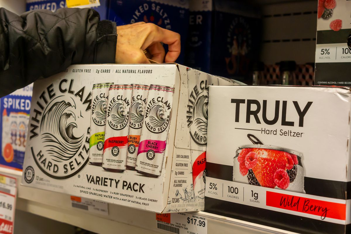 A person pulls a variety pack of White Claw spiked seltzer from a grocery store shelf