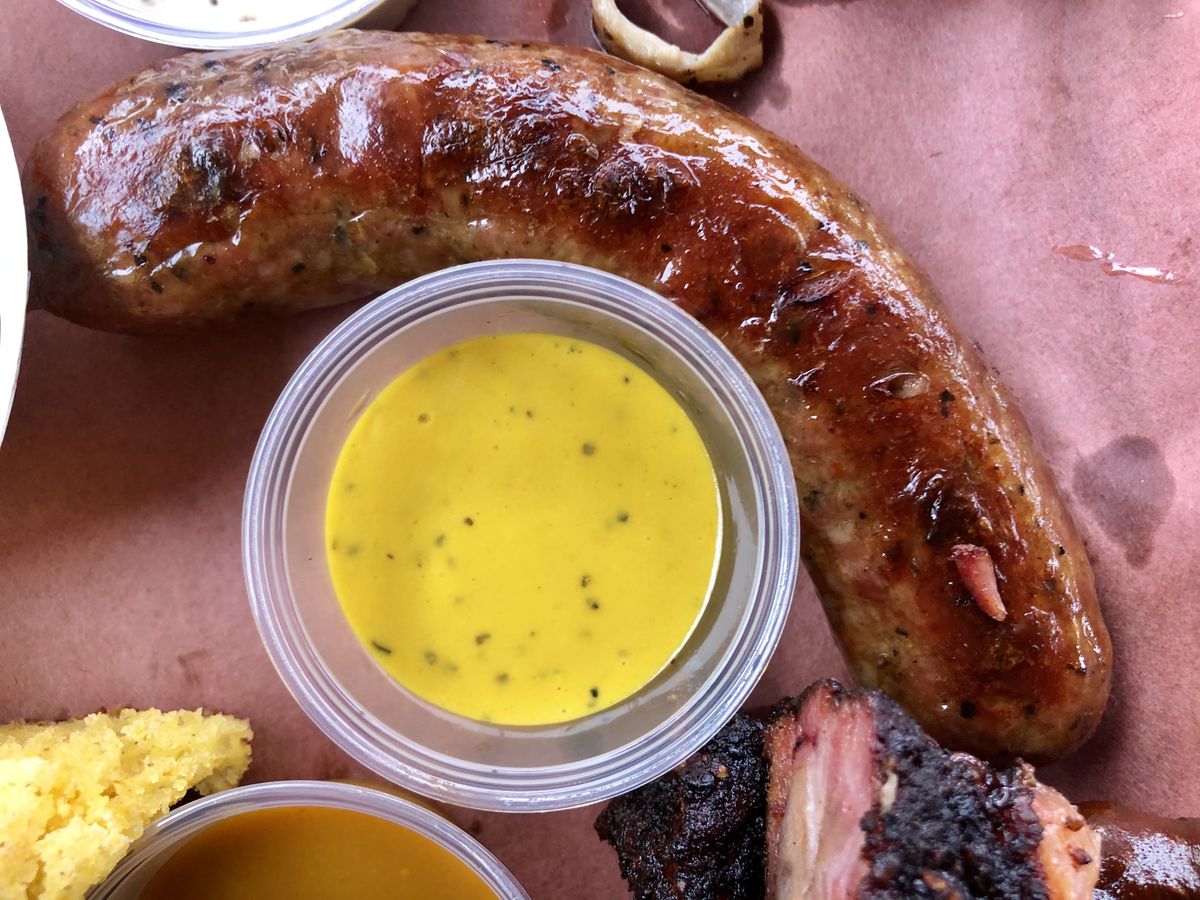 A picture of a sausage with mustard sauce, curled around the container of sauce