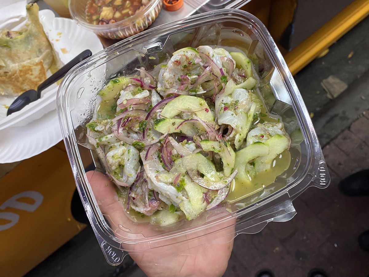 A hand clutches a plastic container brimming with octopus and slices of cucumber and red onion.