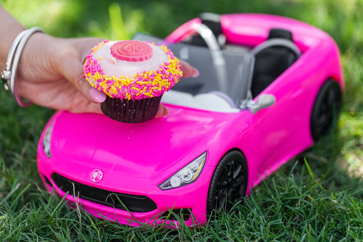 A pink cupcake with sprinkles atop a hot pink Barbie convertible toy.