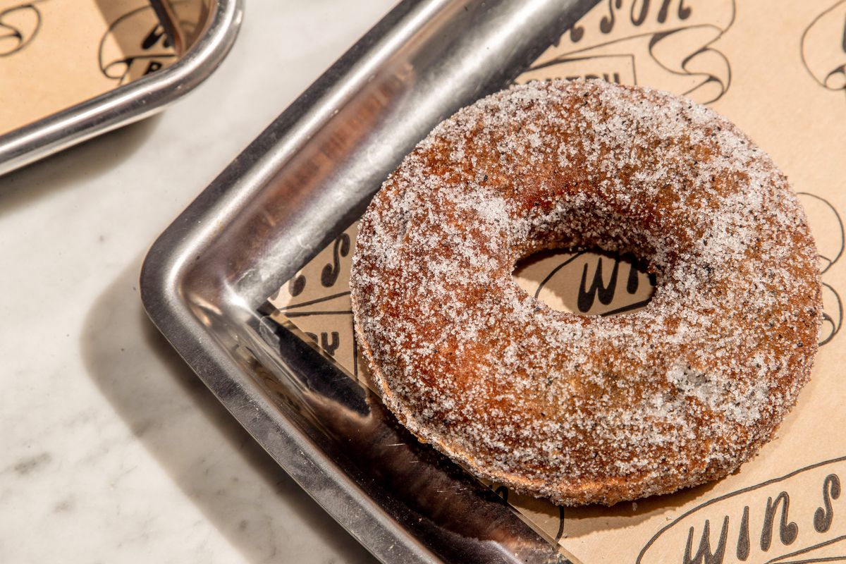 A black sesame sugar-crusted mochi-millet doughnut on a stainless steel tray