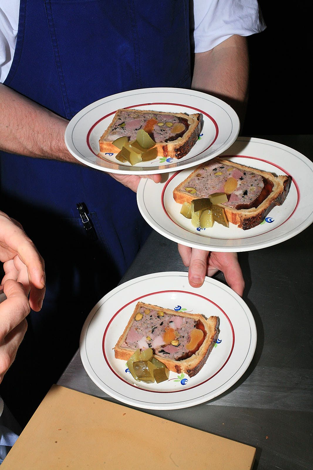 Three plates of paté en croute being carried at once.