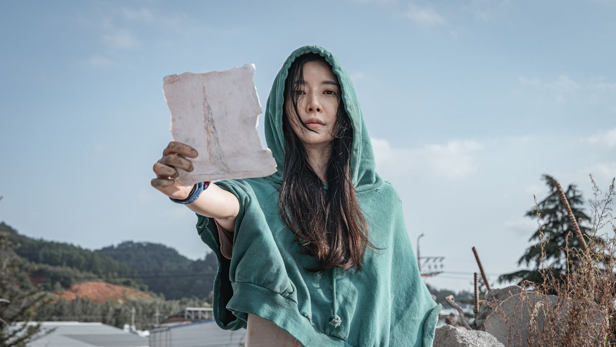 A woman in a green hoodie holds up a piece of paper in Sweet Home.