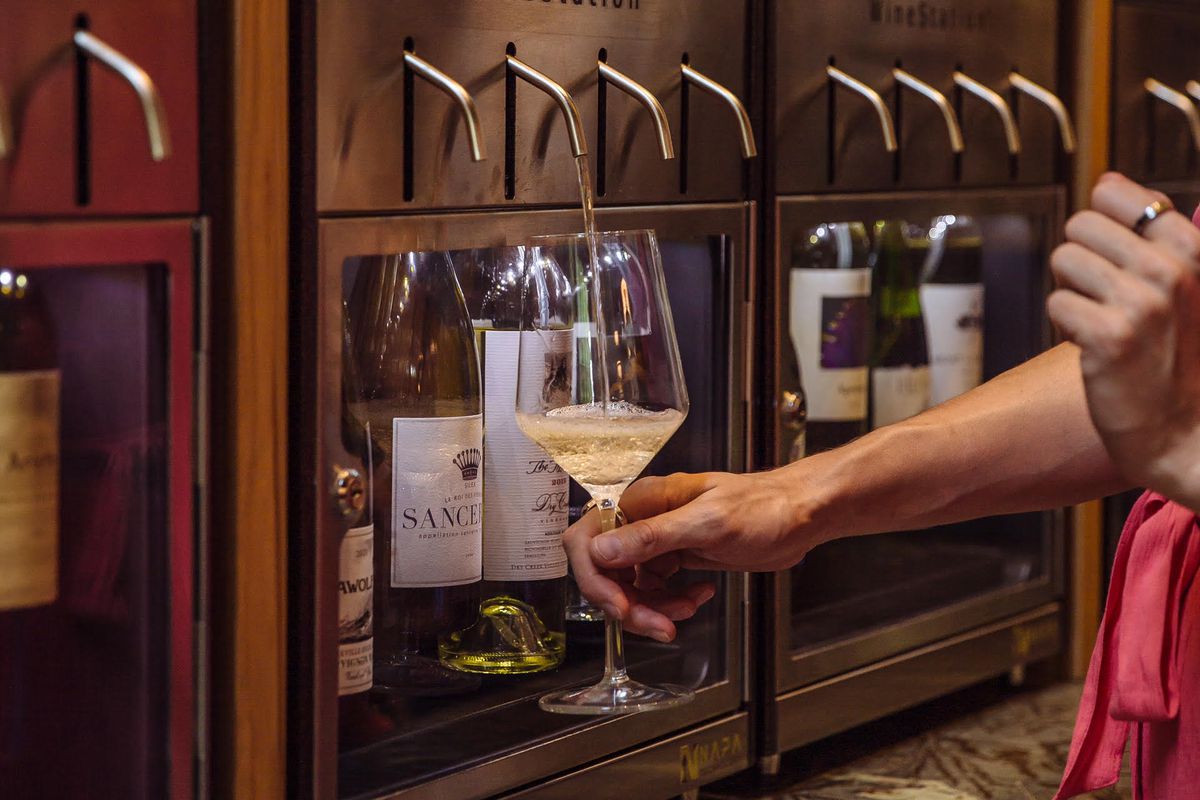 A person holds a wine glass under a machine that dispenses tastes.