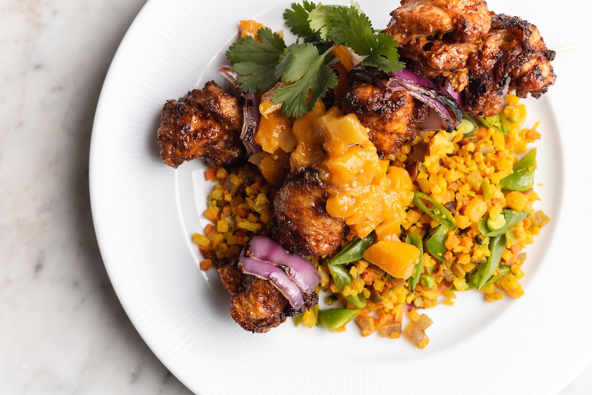 A plate of baked chicken tikka masala skewers with roasted vegetables, Bombay cashew rice, and mango mustard seed chutney