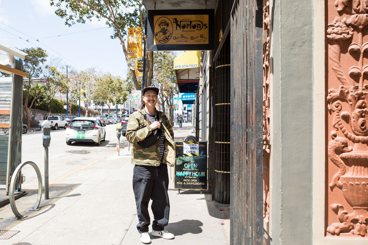 A man stands under a sign that says “Emperor Norton’s.”